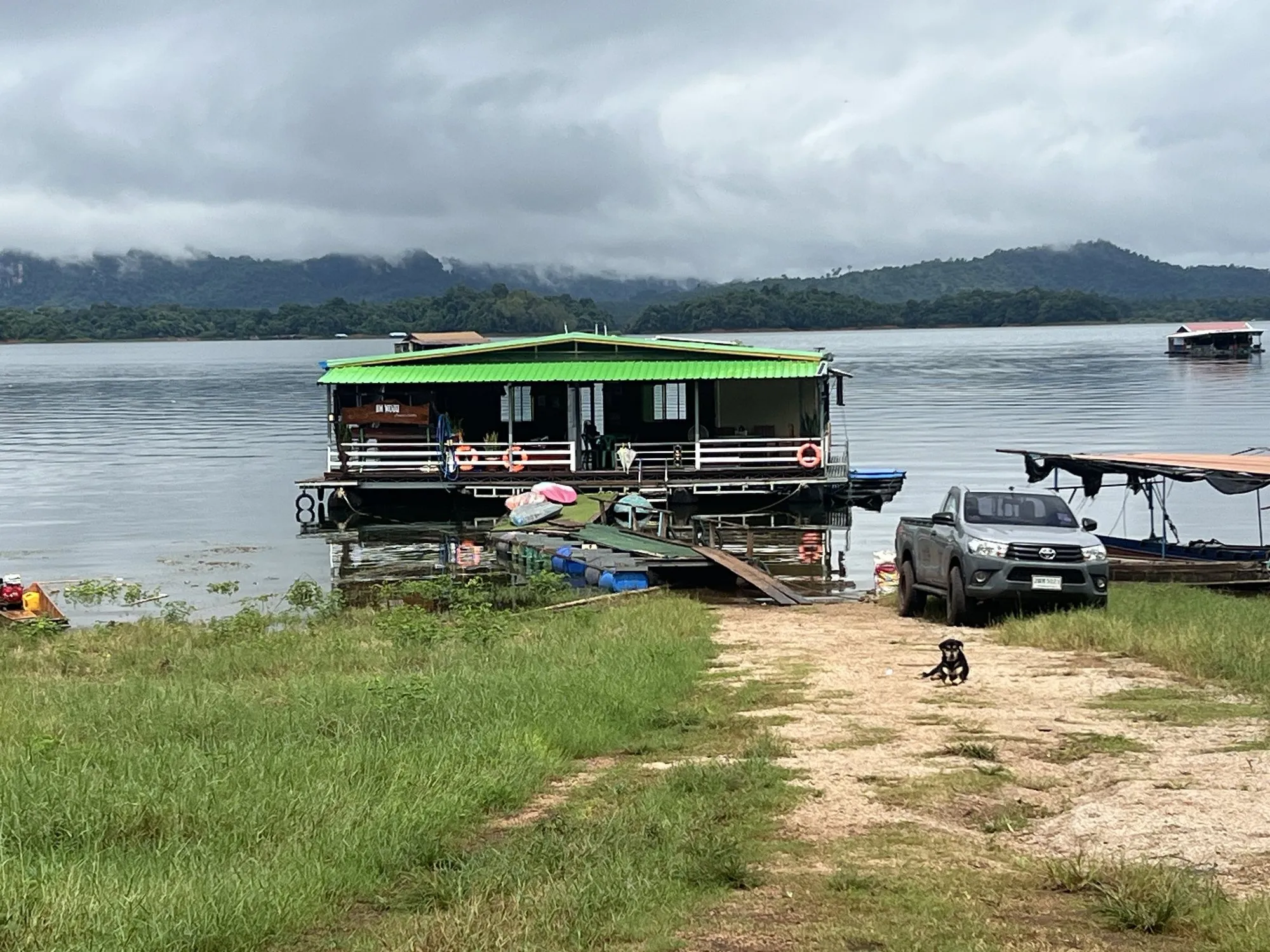 A wooden raft house tied up at the grassy shore of Khao Laem Lake, Kanchanaburi, Thailand.